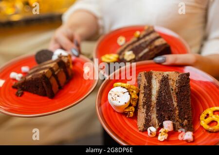 Ein Kellner servierte zwei Stück Kuchen auf Tellern. Er hält zwei Teller mit einer Hand Stockfoto