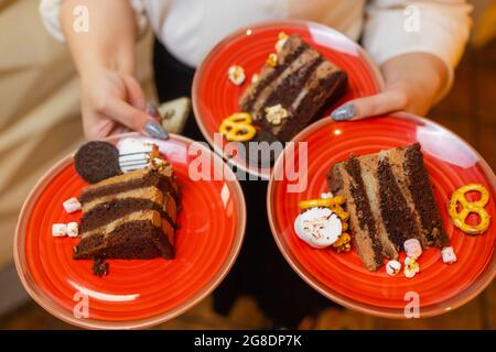 Ein Kellner servierte zwei Stück Kuchen auf Tellern. Er hält zwei Teller mit einer Hand Stockfoto