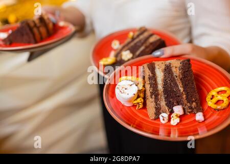 Ein Kellner servierte zwei Stück Kuchen auf Tellern. Er hält zwei Teller mit einer Hand Stockfoto