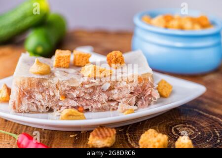 Fleisch mit Rind- und Schweinefleisch auf einer weißen Untertasse. Kalte Vorspeise mit Zwieback und Gurke. Nahaufnahme. Stockfoto