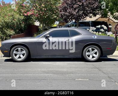 FRESNO, USA - 07. Jul 2021: Ein grauer Sportwagen, der am Bordstein mit wunderschönen Bäumen hinter dem Hotel in Fresno, Kalifornien, USA, geparkt ist Stockfoto