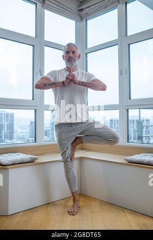 Grauhaariger Mann in einem weißen T-Shirt, der Balance-Asana macht Stockfoto