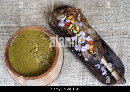 Draufsicht auf köstliche grüne Suppe, serviert in einer Holzschüssel neben einem Lammkotelett mit Paprika darauf Stockfoto