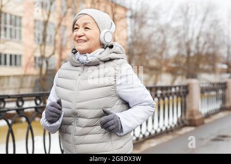 Porträt einer aktiven älteren Frau, die im Winter im Freien läuft und fröhlich lächelt, Platz kopieren Stockfoto