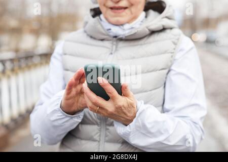 Beschnittenes Porträt einer modernen älteren Frau, die im Winter das Smartphone im Freien hält und Platz zum Kopieren verwendet Stockfoto