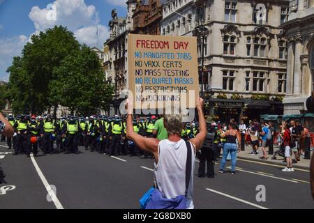 London, Großbritannien. Juli 2021. Ein Protestler hält während der Demonstration in der Parliament Street ein Anti-Restriktionen-Plakat zum Freedom Day vor der Polizei.Demonstranten versammelten sich am Freedom Day, dem Tag, an dem die meisten Beschränkungen des Coronavirus in England aufgehoben wurden, um gegen die COVID-19-Impfung zu protestieren, Impfpass und alle verbleibenden Beschränkungen. Kredit: SOPA Images Limited/Alamy Live Nachrichten Stockfoto