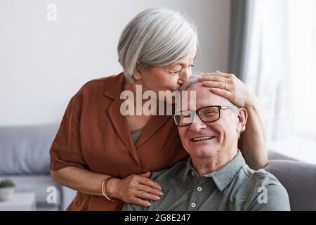 Porträt eines glücklichen älteren Ehepaares, das sich umarmt und die Frau den Mann auf die Stirn küsst Stockfoto