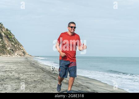 Ein Jogger, der mit seinem Hund am Strand entlang läuft Stockfoto