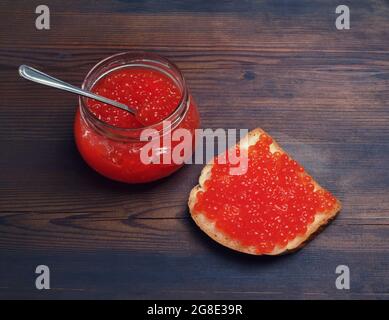 Sandwich mit rotem Kaviar, Glas und Löffel auf Vintage-Holztisch Hintergrund. Stillleben mit rotem Kaviar. Stockfoto