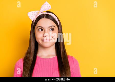 Foto von niedlichen hübschen kleinen Schulmädchen gekleidet rosa T-Shirt suchen leeren Raum lächelnd isoliert gelbe Farbe Hintergrund Stockfoto