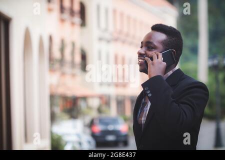 Glücklich lächelnder professioneller afrikanischer Mann mit Smartphone. Geschäftsmann hält und spricht mit einem mobilen Smartphone Stockfoto