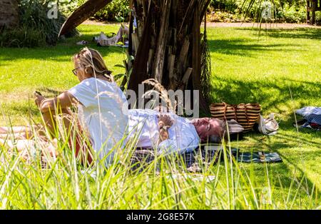 Ein Paar, das weiße Sommerkleidung trägt, entspannt sich im Chelsea Physic Garden in London auf dem Rasen. Stockfoto