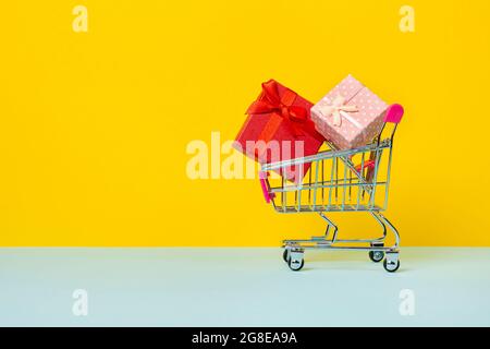 Spielzeug-Einkaufswagen oder -Trolley mit voll mit Geschenkkartons. Ein Geschenk für einen Feiertag, Jahrestag oder Geburtstag. Trolley-Wagen mit Geschenkkartons isoliert über Stockfoto