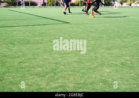 Synthetisches Fußballfeld durch ein Netz gesehen. Das Netz und die Schatten, die es wirft, bilden Muster von Linien, die Diamanten bilden. Sport und Geometrie Hintergrund. Stockfoto