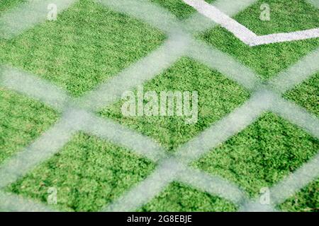 Synthetisches Fußballfeld durch ein Netz gesehen. Das Netz und die Schatten, die es wirft, bilden Muster von Linien, die Diamanten bilden. Sport und Geometrie Hintergrund. Stockfoto