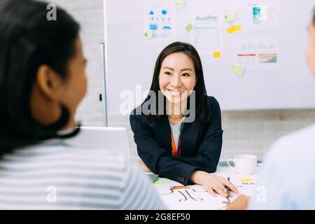 Asiatische ausgereifte Frau lächelnd und andere Geschäftsleute während der Konferenz sitzen. Smart mittleren Alter Dame Diskussion haben. Stockfoto
