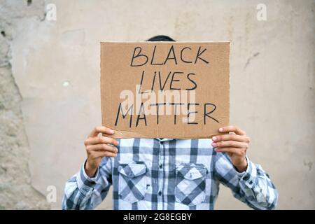 Mann, der Karton mit der Aufschrift hält, hat schwarzes Leben Wert. Der Kaukasier zeigt mit einem Plakat seinen Protest vor dem Hintergrund einer Zementwand Stockfoto