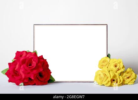 Holzrahmen um ein leeres Bild auf weißem Hintergrund mit zwei Blumensträußen aus roten und gelben Rosen Stockfoto