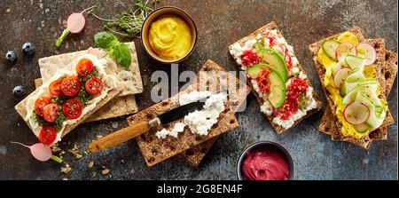 Draufsicht auf verschiedene leckere Knäckebrot-Toasts mit frischem Gemüse auf dunklem Tisch im Studio angeordnet Stockfoto