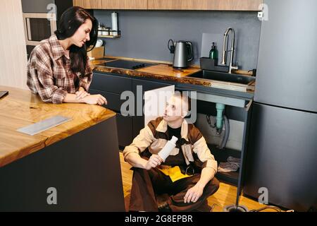 Junge Frau im Gespräch mit Klempner mit Stück Rohr während der Reparaturarbeiten Stockfoto