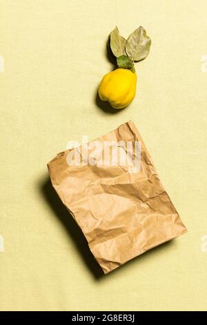 Ein Bio-Quitten-Apfel und ein gebrauchter Papierbeutel auf faltenem pastellfarbenem Leinenhintergrund. Frucht hat natürliche Unvollkommenheiten. Bewusste Konsumer Stockfoto