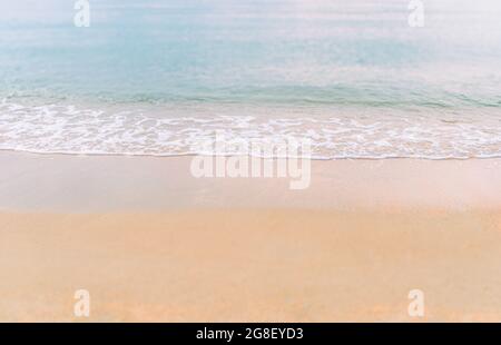 Kleine Welle mit den kleinen weißen Blasen an einem goldenen Strand im Sonnenuntergang, verschwommene Vorder- und Rückseite, schöne Farbe am Meer. Stockfoto