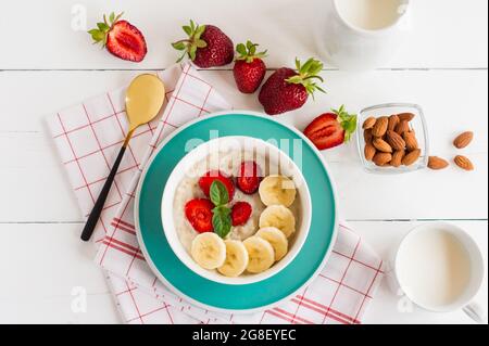 Haferflocken mit Erdbeeren und Bananenscheiben auf einem weißen Teller, der auf einem weißen Holztisch steht Stockfoto