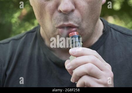 Gesicht eines Mannes, der eine elektronische Zigarette raucht. Mann mit Dampfvorrichtung und Rauchausatmend. Verdampfung, Verdampfung einer Flüssigkeit zum Einatmen Stockfoto