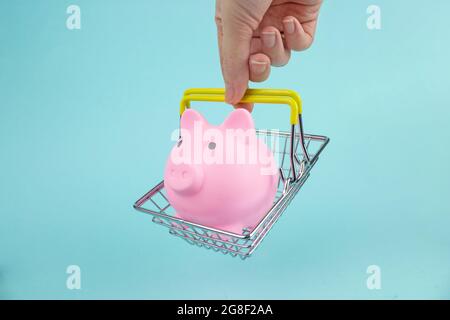 Einkaufskonzept. Hand hält den Warenkorb mit Sparschwein auf blauem Hintergrund. Saisonale Rabatte Stockfoto
