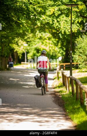 Frau, die im Sommer auf einem Radweg mit dem Fahrrad unterwegs ist Stockfoto