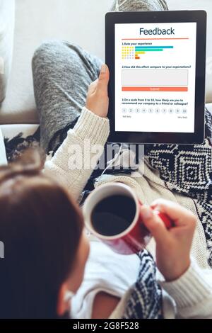 Eine junge Frau schreibt eine Kundenbewertung und hinterlässt eine Bewertung auf dem Tablet. Kundenerfahrung und Feedback-Konzept. Stockfoto
