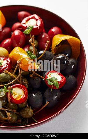 Eingelegtes Gemüse auf einem Teller, Oliven, schwarze Oliven, gefüllte Paprika, Radieschen. Verschiedene Gemüsesorten, Gemüse mit Gewürzen in Öl-Nahaufnahme. Stockfoto