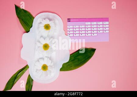 Konzept der Menstruationszeit. Menstruationskalender mit hygienischen Tampons, Damenbinden, Blumen auf rosa Hintergrund Draufsicht Platz für Text. Stockfoto