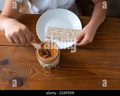 Kind Verbreitung Erdnussbutter auf Knäckebrot Essen Sandwich Holztisch Haus kitchen.School Mädchen mit Brot Scheibe Vollkorn Snack.Kid Kochen Frühstück Stockfoto