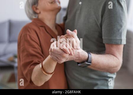 Beschnittenes Porträt eines liebenden älteren Paares, das zu Hause tanzt und die Hände hält Stockfoto