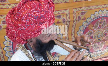 Älterer indischer Mann in traditioneller Kleidung und Turban, der auf zwei Bansuris spielt Stockfoto