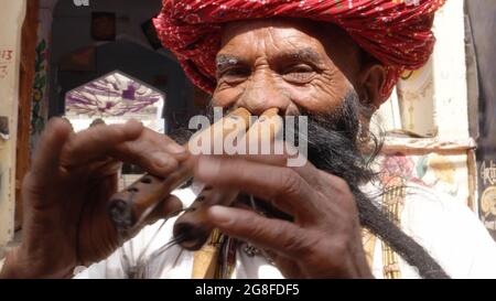 Älterer indischer Mann in traditioneller Kleidung und Turban, der auf zwei Bansuris spielt Stockfoto