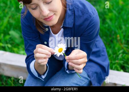 Die hübsche junge Frau im blauen Hemd erraten auf einer Kamille auf der Wiese. Selektiver Fokus. Nahaufnahme Stockfoto