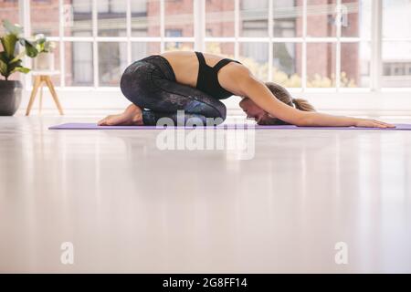 Junge Frau, die Yoga praktiziert, Kinder posieren. Weibliche Entspannung in Balasana im Fitnessstudio. Stockfoto