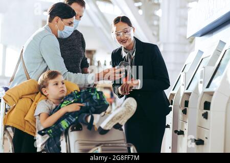 Ein Paar zeigte dem Flugbegleiter am Flughafen das Handy, der Sohn saß auf dem Gepäckwagen. Bodenwächter, der die Familie des Reisenden bei der Selbstbedienung unterstützt Stockfoto