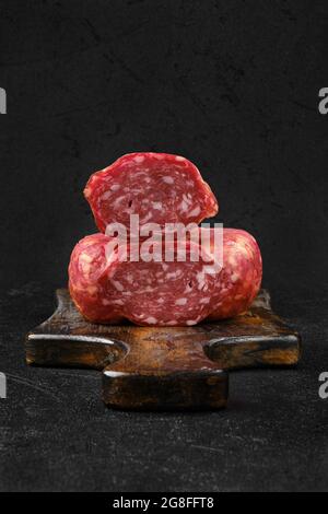 Nahaufnahme von geräucherter Rinderwurst auf Schneidebrett auf schwarzem Hintergrund Stockfoto