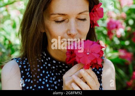 Porträt einer jungen kaukasischen Frau mit rosa Blüten in den Haaren und Händen Stockfoto