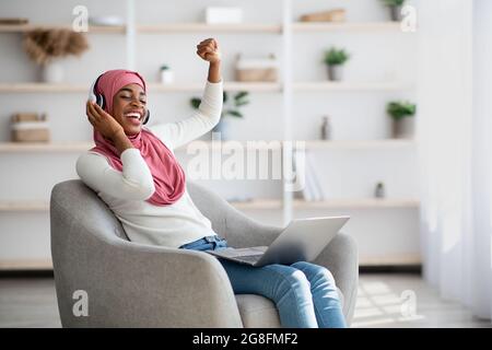 Überglücklich Schwarze Islamische Dame In Kabellosen Kopfhörern Musik Online Auf Laptop Hören Stockfoto