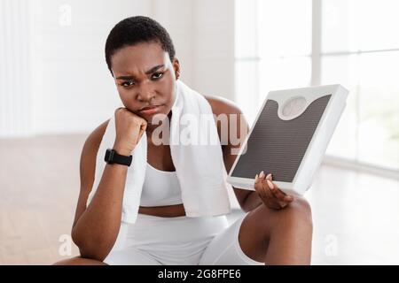 Porträt einer unglücklichen afrikanischen Frau, die eine Waage im Bad hält Stockfoto