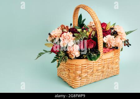 Ein schöner Blumenstrauß in einem gelben Korbkorb steht auf blauem Hintergrund. Leer für eine Grußkarte. Verschiedene Sommerblumen. Stockfoto