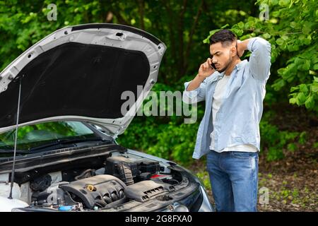 Trauriger arabischer Mann, der den Motor ansah und den Autoservice anrief Stockfoto