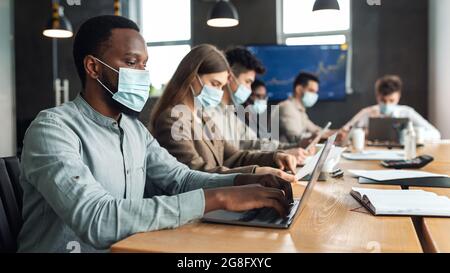 Kollegen, die am Startup-Projekt arbeiten, tragen Gesichtsmasken mit Hilfe von Technologie Stockfoto
