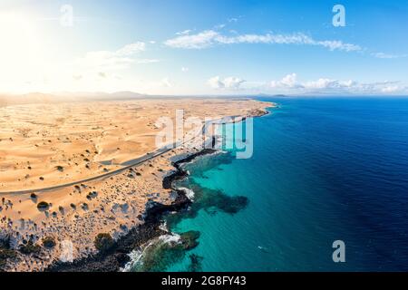 Luftaufnahme einer leeren Straße neben dem kristallklaren türkisfarbenen Meer und Sanddünen, Corralejo, Fuerteventura, Kanarische Inseln, Spanien, Atlantik, Europa Stockfoto