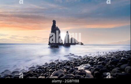 Wellen schlagen am vulkanischen Steinstrand und den Meeresstapeln von Ilheus da Rib und Ribeira da Janela bei Sonnenaufgang, auf der Insel Madeira, Portugal, im Atlantik, in Europa Stockfoto