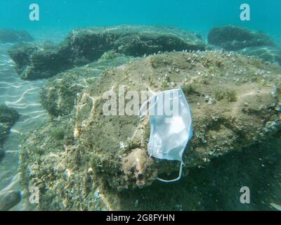 Ausrangierte chirurgische Gesichtsmaske, die auf kontaminiertem Meeresökosystem schwimmt, kovid19 Umweltverschmutzung Stockfoto